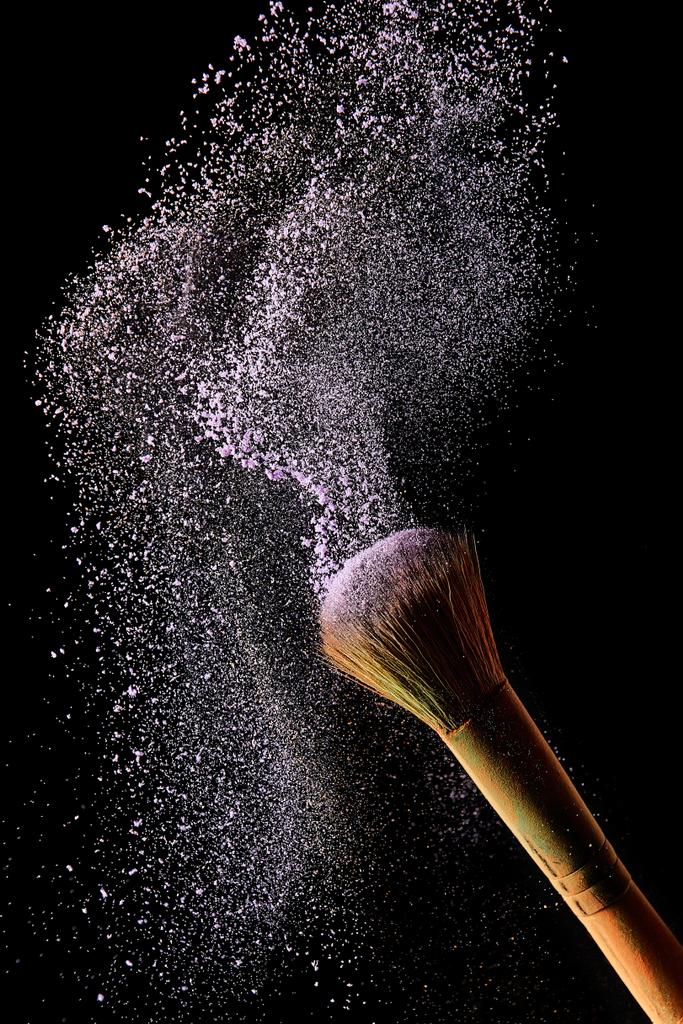 cepillo cosmético con explosión de polvo violeta sobre fondo negro
 - Foto, Imagen