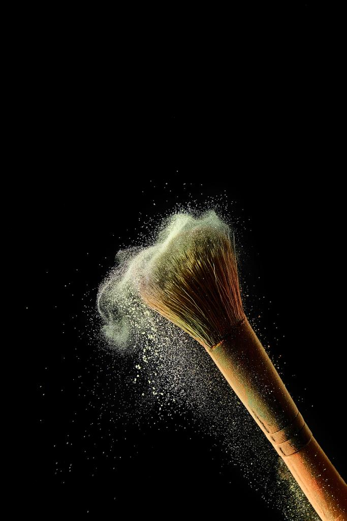 cosmetic brush with yellow colorful scattering powder on black background - Photo, Image
