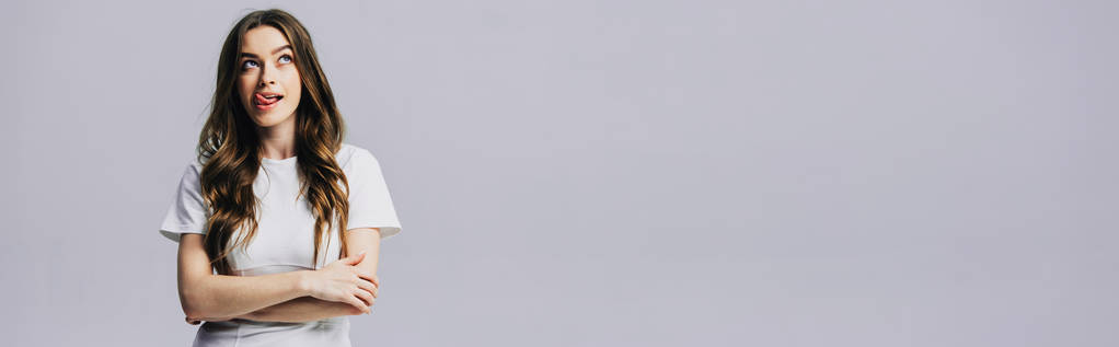 красивая девушка в белой футболке смотрит в сторону и торчит язык изолирован на сером, панорамный снимок
 - Фото, изображение