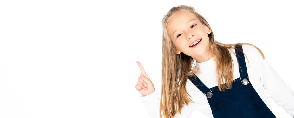 Panoramaaufnahme einer fröhlichen Schülerin, die mit dem Finger zeigt und in die Kamera lächelt, isoliert auf Weiß - Foto, Bild
