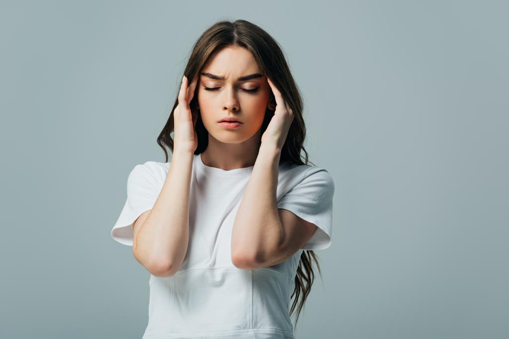 gespannen mooi meisje in wit t-shirt met gesloten ogen lijden aan migraine geïsoleerd op grijs - Foto, afbeelding