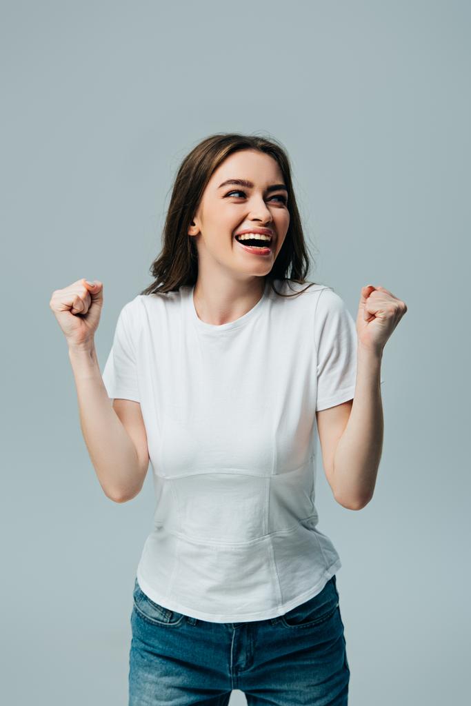 счастливая красивая девушка в белой футболке, показывающая жест "да" и уединяющаяся на сером
 - Фото, изображение