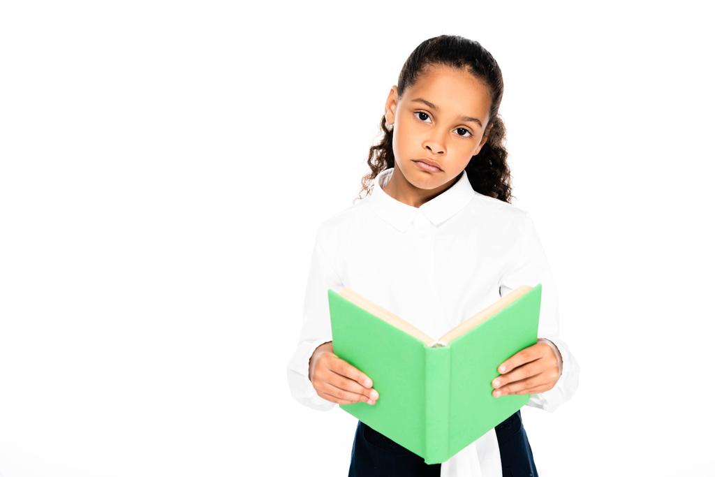 boos African American schoolmeisje kijkt naar camera terwijl holding boek geïsoleerd op wit - Foto, afbeelding