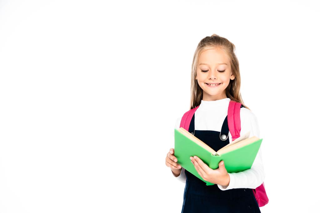 schattig schoolmeisje glimlachen tijdens het lezen boek geïsoleerd op wit - Foto, afbeelding