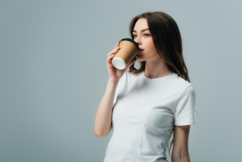krásná dívka v bílém triku, pít kávu a jít izolovaně na šedé - Fotografie, Obrázek