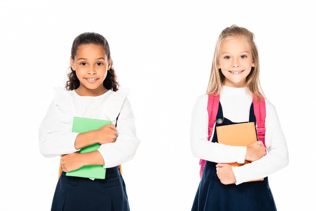 deux écolières multiculturelles mignonnes tenant des livres et souriant à la caméra isolé sur blanc
 - Photo, image