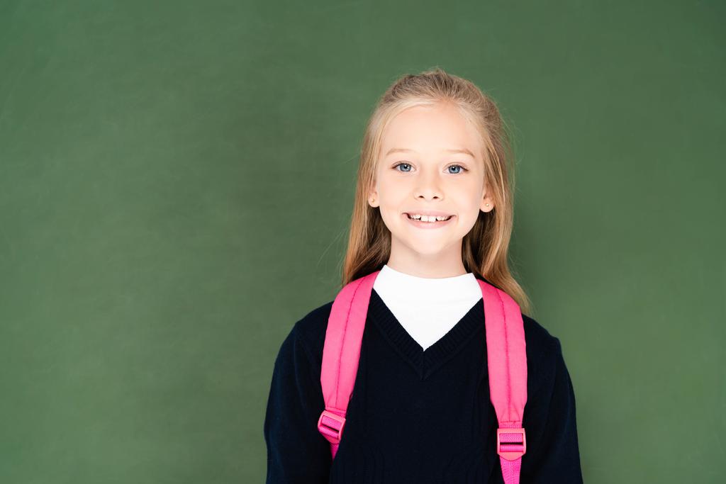 緑の黒板の近くに立っている間、カメラで微笑む陽気な女子高生 - 写真・画像