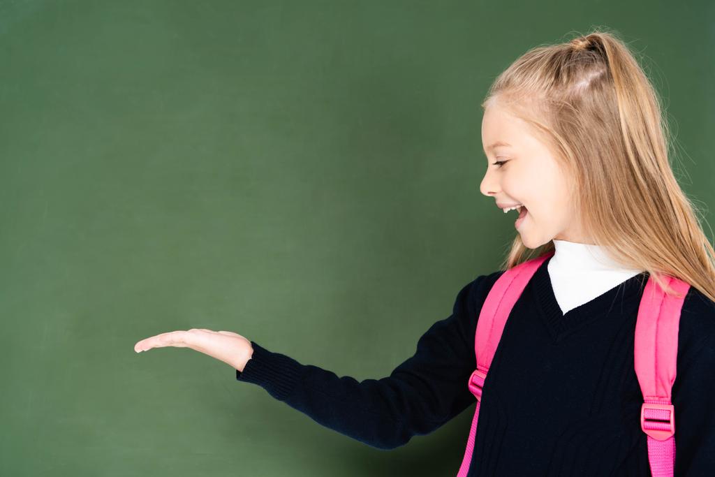 весела школярка вказує рукою на зелену крейдяну дошку
  - Фото, зображення