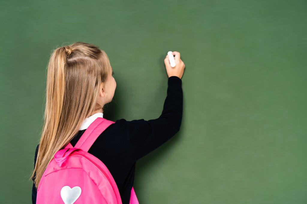 visão traseira da estudante com mochila rosa escrevendo no quadro verde
  - Foto, Imagem