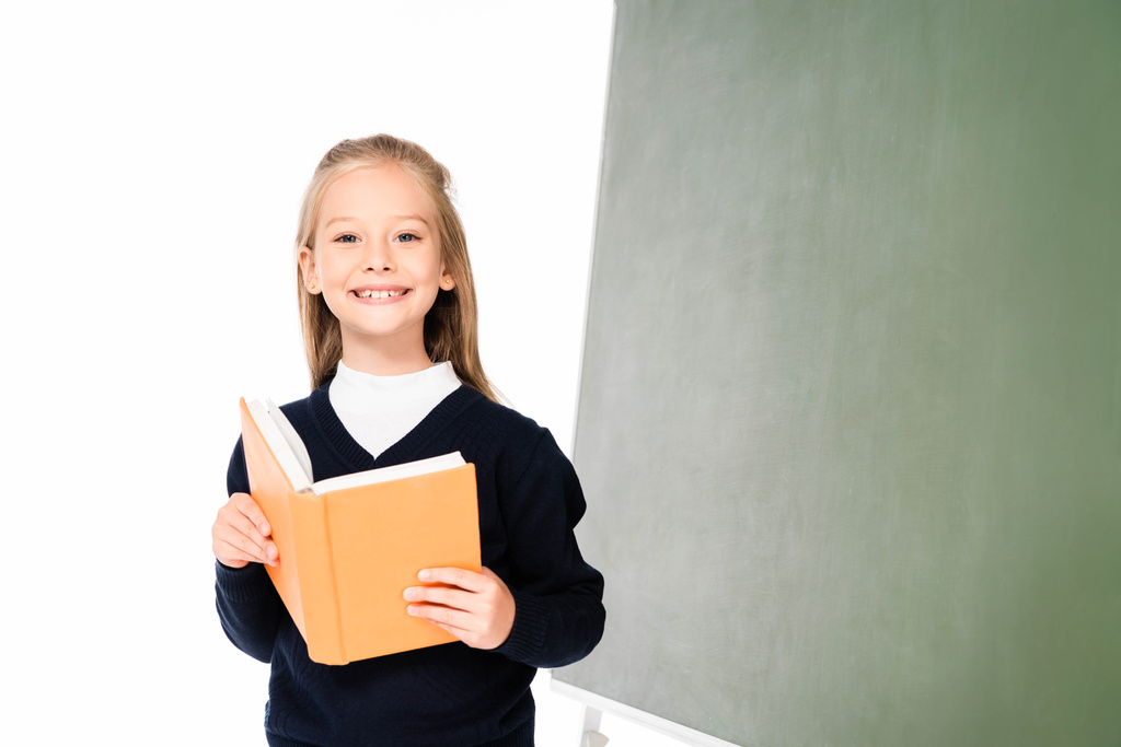 adorabile studentessa sorridente alla macchina fotografica mentre in piedi vicino alla lavagna e tenendo libro isolato su bianco
 - Foto, immagini