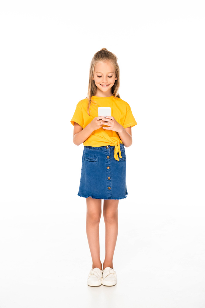 vista completa de un niño lindo y sonriente usando un teléfono inteligente sobre un fondo blanco
 - Foto, Imagen