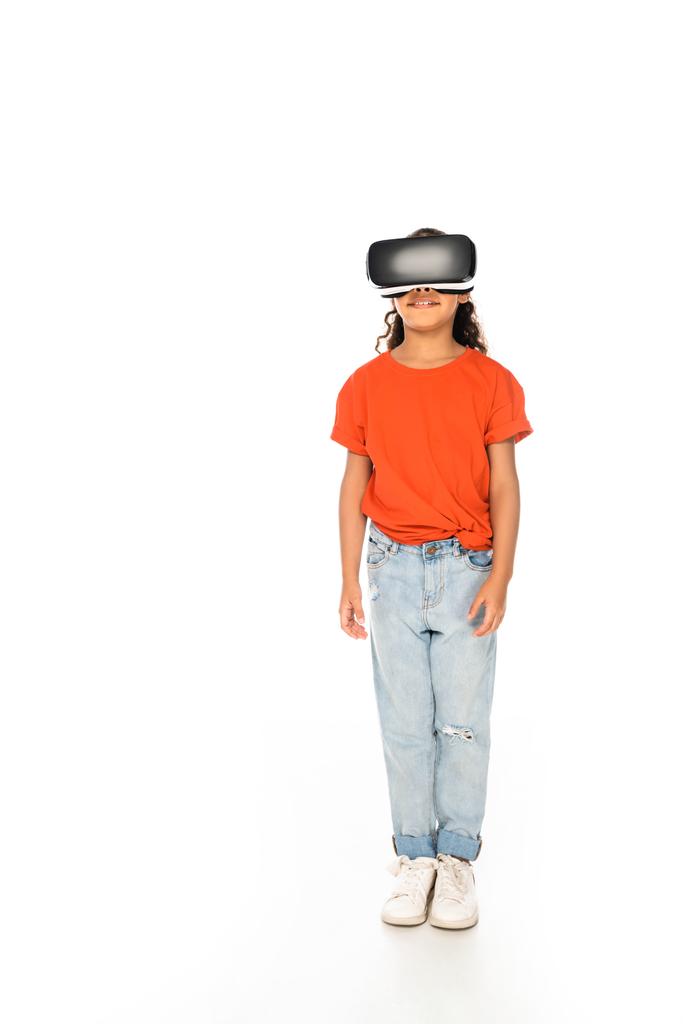 teljes hosszúságú kilátás a mosolygó afro-amerikai gyerek segítségével virtuális valóság headset fehér háttér - Fotó, kép