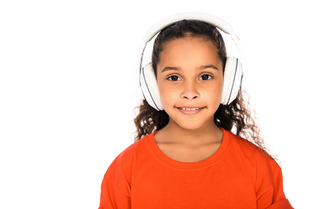 白で隔離されたヘッドフォンで音楽を聴きながらカメラで微笑む愛らしいアフリカ系アメリカ人の子供 - 写真・画像