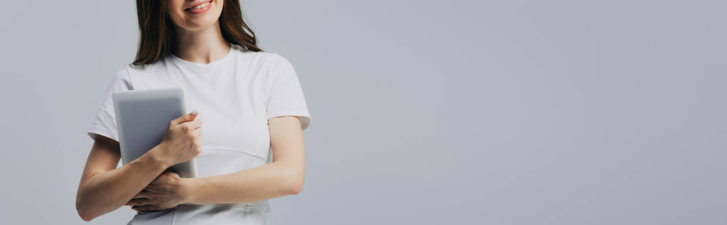 灰色のパノラマショットで隔離されたデジタルタブレットを保持する白いTシャツで幸せな女の子のトリミングされたビュー - 写真・画像