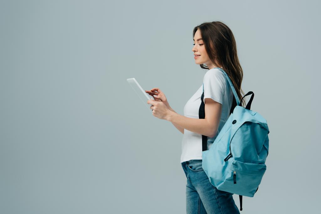 oldalnézetből csinos lány, kék hátizsák segítségével digitális tabletta izolált szürke - Fotó, kép
