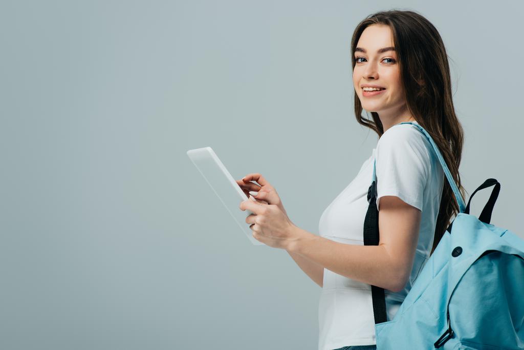 вид збоку досить усміхнена дівчина з блакитним рюкзаком з використанням цифрового планшета ізольовано на сірому
 - Фото, зображення