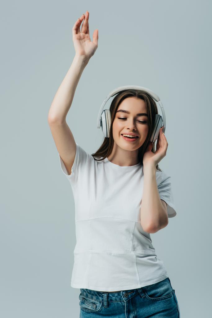szczęśliwy Ładna dziewczyna słuchania muzyki w słuchawkach bezprzewodowych i taniec izolowane na szarym - Zdjęcie, obraz