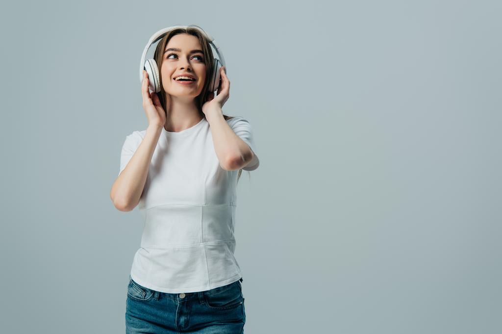 ευτυχισμένο ονειρεμένο κορίτσι ακούγοντας μουσική σε ασύρματα ακουστικά που απομονώνονται σε γκρι - Φωτογραφία, εικόνα