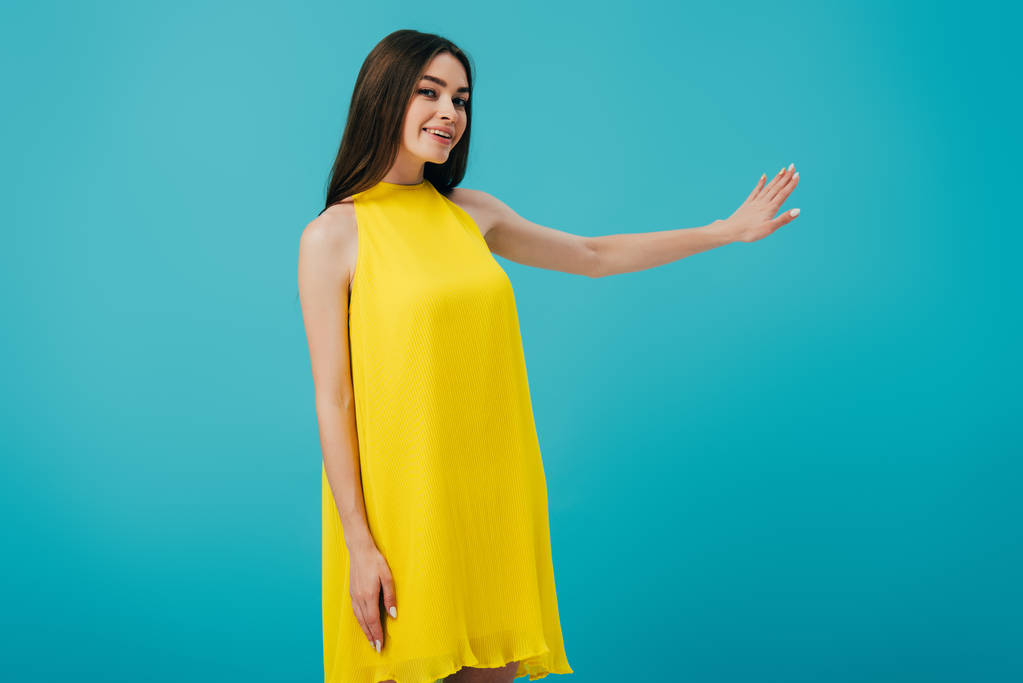feliz hermosa chica en vestido amarillo gesto con la mano aislada en turquesa
 - Foto, Imagen