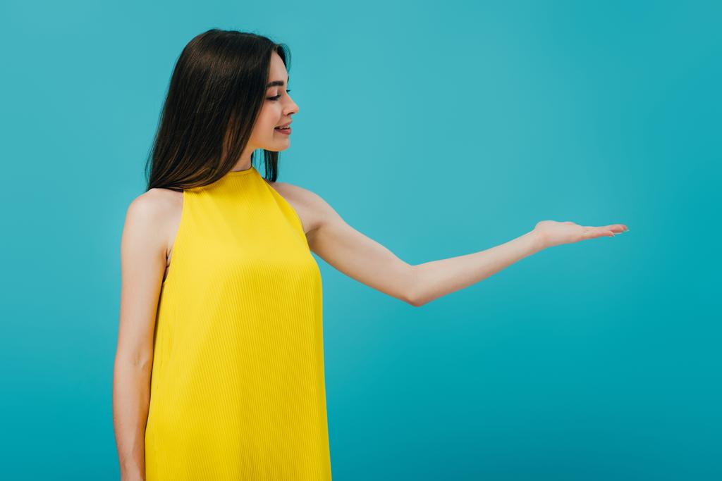 heureuse belle fille en robe jaune pointant avec la main à l'espace de copie isolé sur turquoise
 - Photo, image