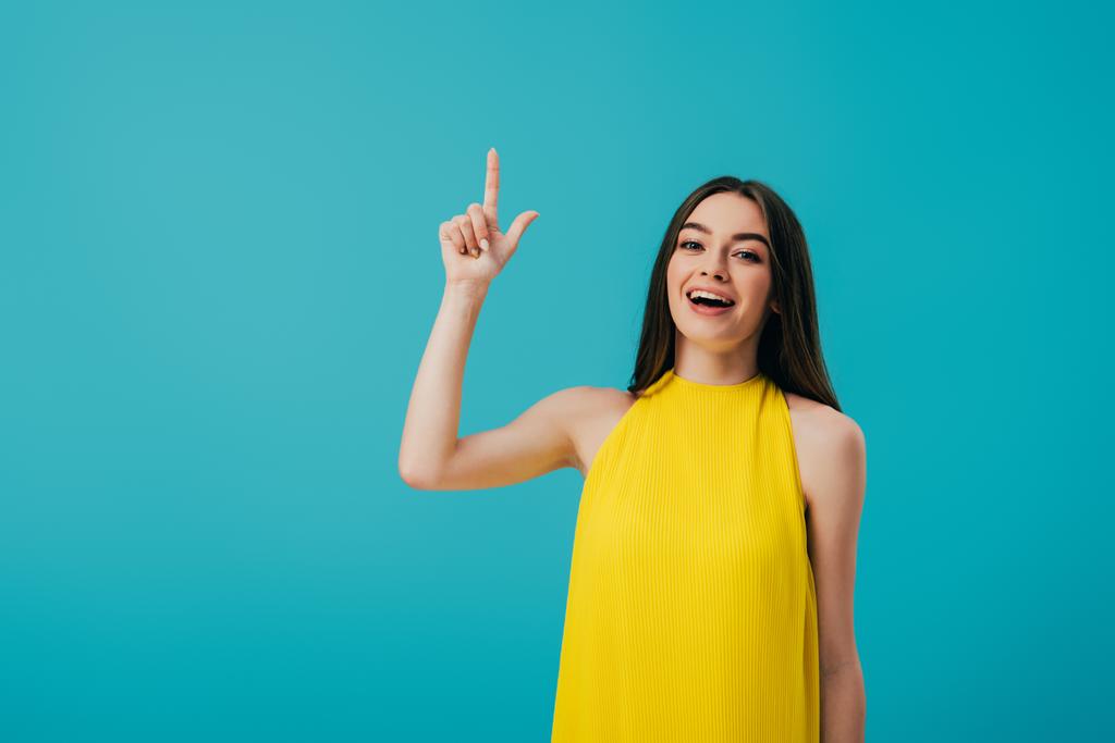 excitada hermosa chica en vestido amarillo apuntando con el dedo hacia arriba aislado en turquesa
 - Foto, imagen