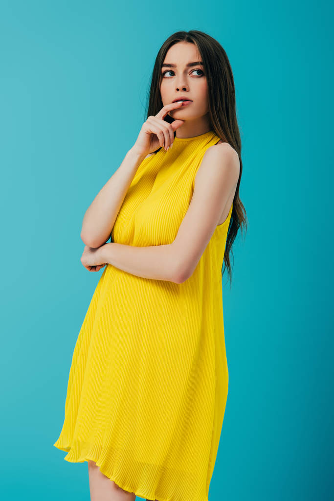 вдумлива красива дівчина в жовтій сукні дивиться ізольовано на бірюзовому
 - Фото, зображення