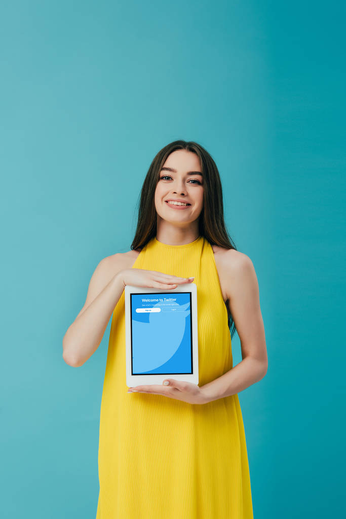 KYIV, UCRAINA - 6 GIUGNO 2019: bella ragazza sorridente in abito giallo che mostra tablet digitale con app twitter isolata su turchese
 - Foto, immagini