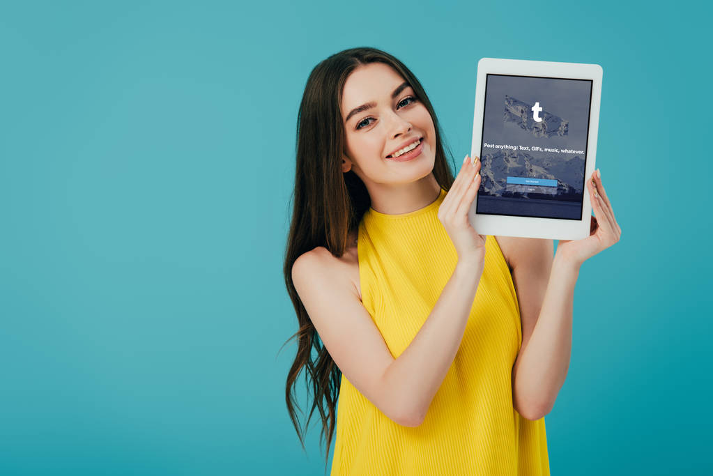 KYIV, UCRAINA - 6 GIUGNO 2019: felice bella ragazza in abito giallo che mostra tablet digitale con app tumblr isolata sul turchese
 - Foto, immagini