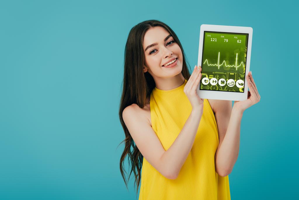 красивая счастливая девушка в желтом платье показывает цифровой планшет с приложением здравоохранения изолированы на бирюзовой
 - Фото, изображение