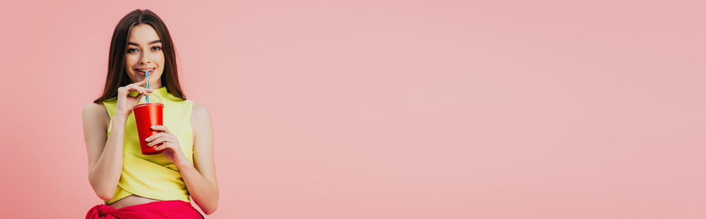 bella ragazza sorridente in abiti luminosi bere soda da paglia isolata su rosa, caldo panoramico
 - Foto, immagini