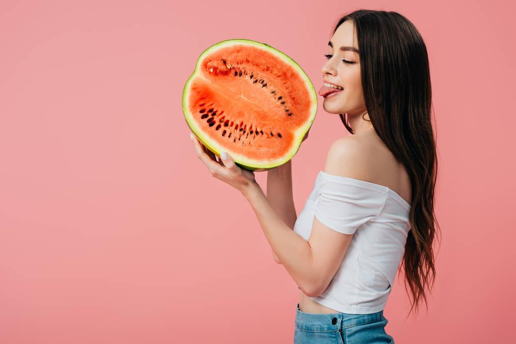 krásná usmívající se dívka olizuje zralý lahodný meloun napůl izolovaný na růžovém - Fotografie, Obrázek