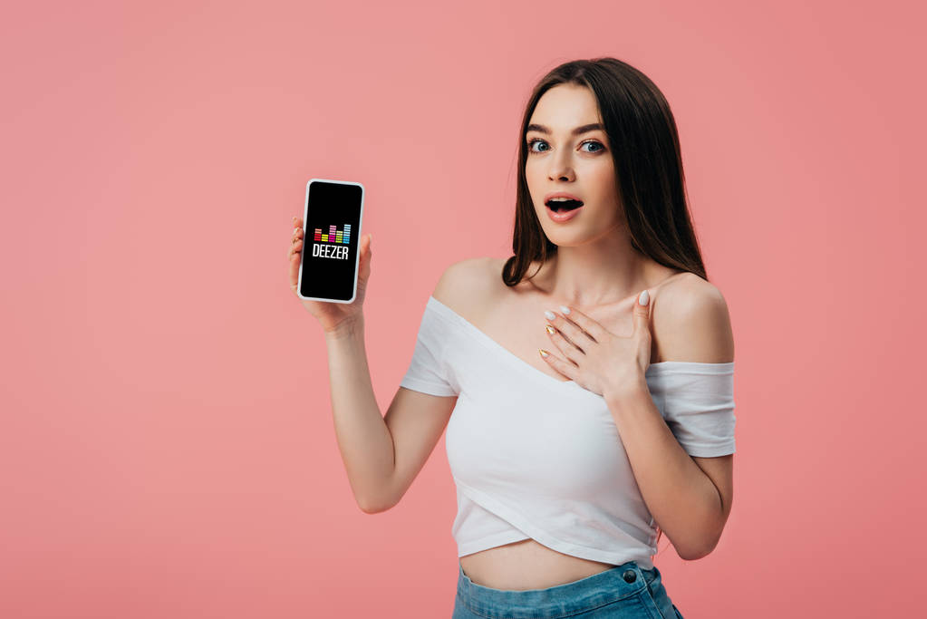 KYIV, UKRAINE - kesäkuu 6, 2019: kaunis järkyttynyt tyttö, jolla on älypuhelin, jossa on vaaleanpunainen eristetty deezer-sovellus
 - Valokuva, kuva
