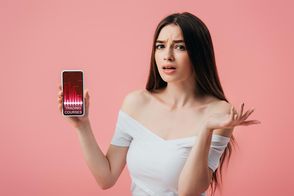 bella ragazza confusa in possesso di smartphone con corsi di trading app e mostrando gesto scrollata di spalle isolato su rosa
 - Foto, immagini