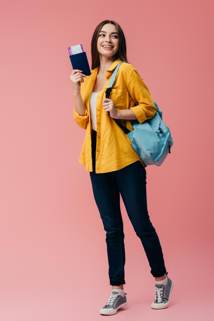 piena lunghezza vista di bella ragazza sorridente con zaino in possesso di passaporto con biglietto aereo isolato su rosa
 - Foto, immagini