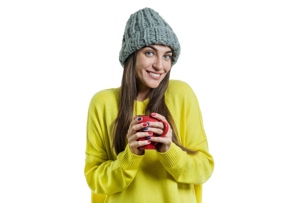 Portrait d'hiver de jeune femme souriante positive en pull, bonnet tricoté avec tasse de boisson chaude, fond blanc isolé
 - Photo, image