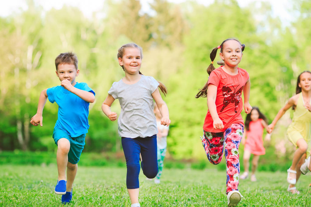 Monet eri lapset, pojat ja tytöt juoksevat puistossa aurinkoisena kesäpäivänä rennoissa vaatteissa.
. - Valokuva, kuva