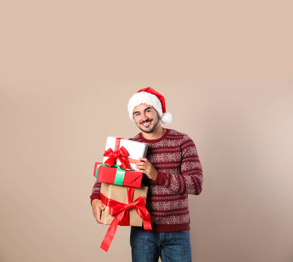 Hombre feliz en jersey de Navidad y Santa sombrero sosteniendo cajas de regalo sobre fondo beige
 - Foto, Imagen