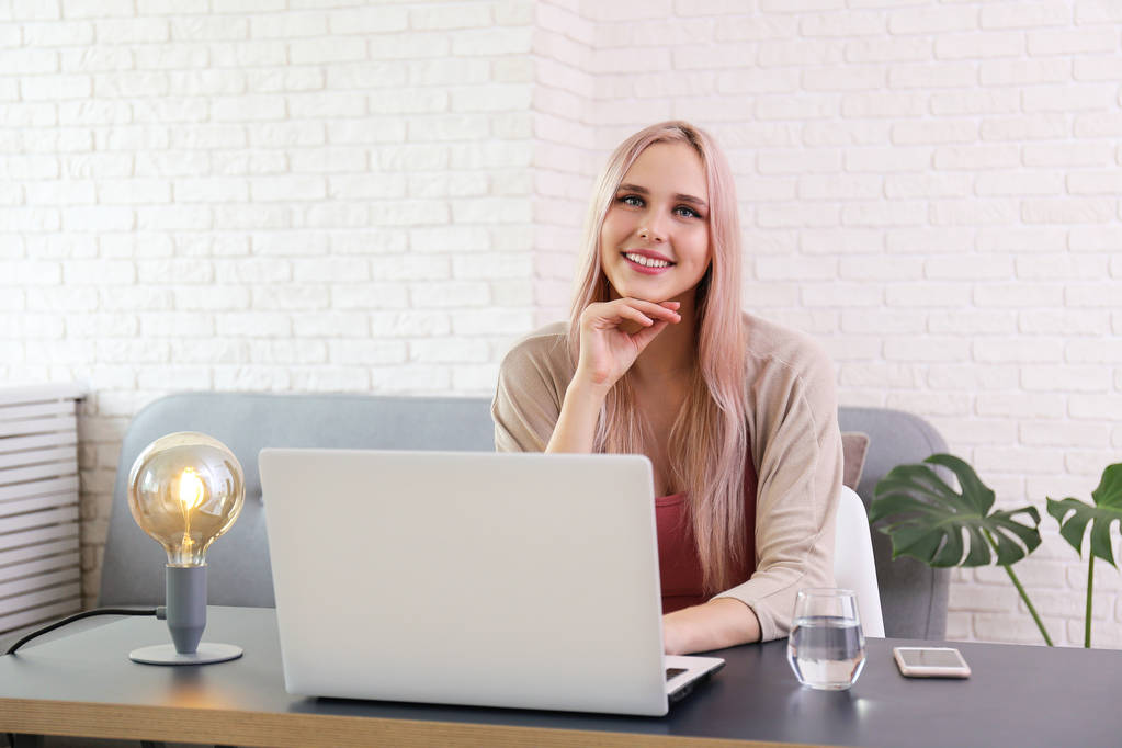 Jonge mooie blonde vrouw met roze haar Toner zittend op haar werkplek met witte laptop. Portret van tiener vrouwelijk model in hoek kantoor interieur. Close-up, kopieer ruimte, achtergrond. - Foto, afbeelding