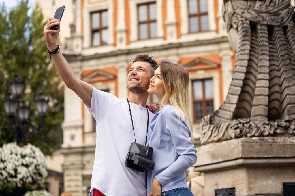 Travel selfie ζευγάρι λήψη φωτογραφία με το τηλέφωνο στην ιστορική πόλη. Ευρώπη καλοκαιρινές διακοπές νέοι άνθρωποι χαμογελούν. Ταξιδάκι με σακίδιο. Υψηλή ανάλυση.  - Φωτογραφία, εικόνα