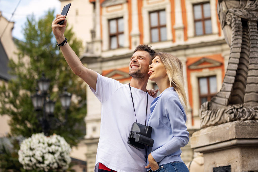 Travel selfie ζευγάρι λήψη φωτογραφία με το τηλέφωνο στην ιστορική πόλη. Ευρώπη καλοκαιρινές διακοπές νέοι άνθρωποι χαμογελούν. Ταξιδάκι με σακίδιο. Υψηλή ανάλυση.  - Φωτογραφία, εικόνα