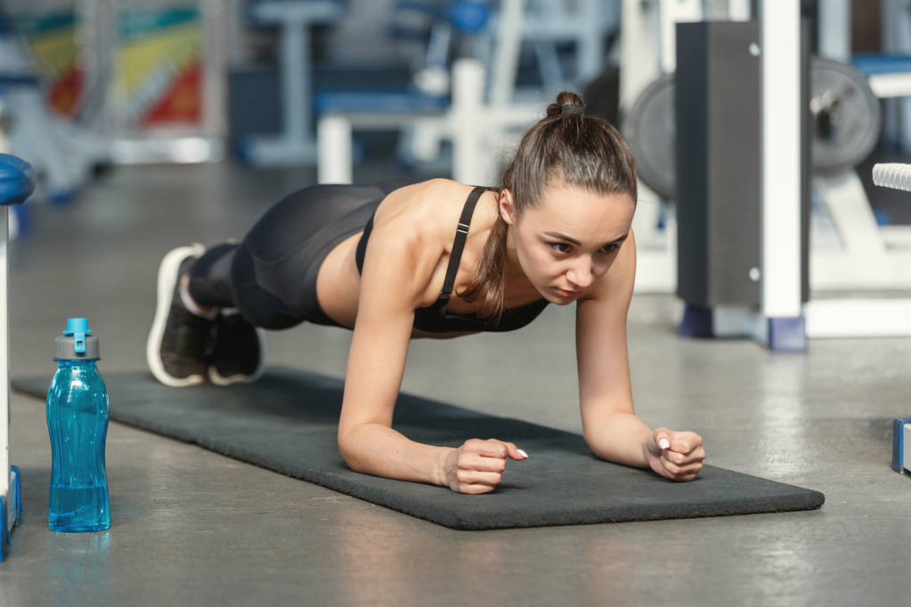 Jovem mulher esportiva fazendo exercício de prancha em um ginásio
 - Foto, Imagem