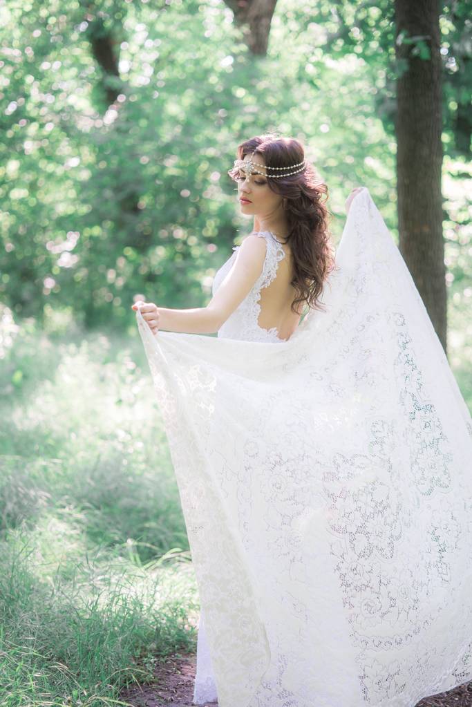 Muchacha joven atractiva en un vestido blanco largo con un hermoso peinado, con una bufanda vintage de encaje blanco en un parque de verano
 - Foto, Imagen