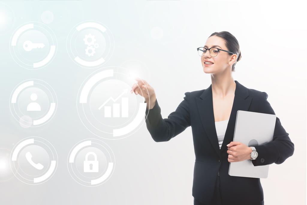 femme d'affaires souriante tenant un ordinateur portable et pointant du doigt les icônes de sécurité et les pictogrammes multimédias sur fond gris
 - Photo, image