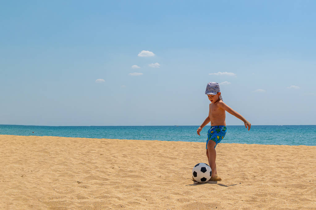 Το παιδί παίζει ποδόσφαιρο στην παραλία. Η έννοια του αθλητισμού και του υγιεινού τρόπου ζωής. Φρέσκος θαλάσσιος αέρας και καλή οικολογία. Αντιγραφή χώρου. - Φωτογραφία, εικόνα