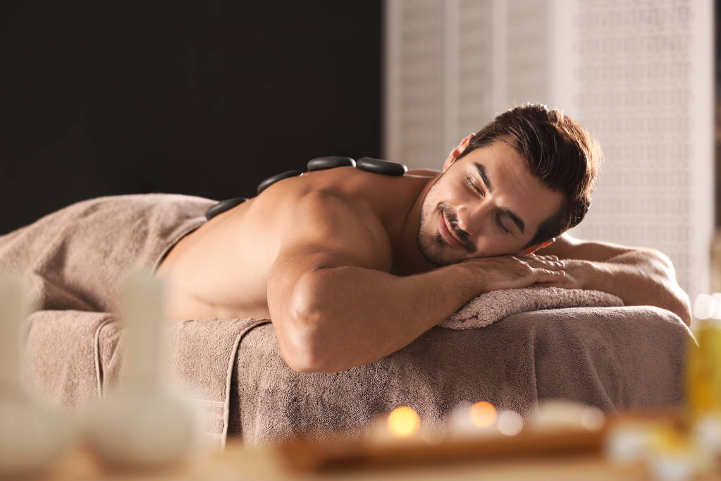 Handsome young man receiving hot stone massage in spa salon - Photo, Image