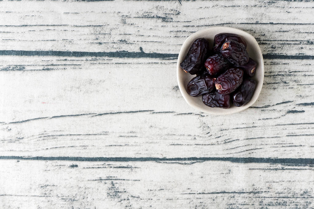 seco dátiles de color azul oscuro frutas en plato hondo, superficie de mesa de madera gris
  - Foto, imagen