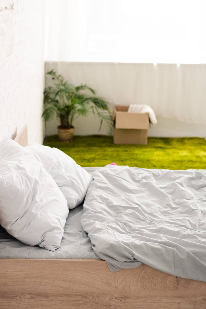 Lit avec linge de lit blanc près du tapis vert avec boîte en carton
 - Photo, image
