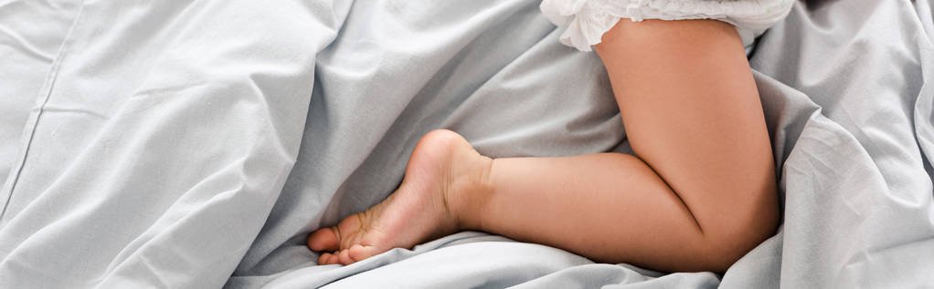 Panoramic shot of cute barefoot baby leg on white sheets - Photo, Image