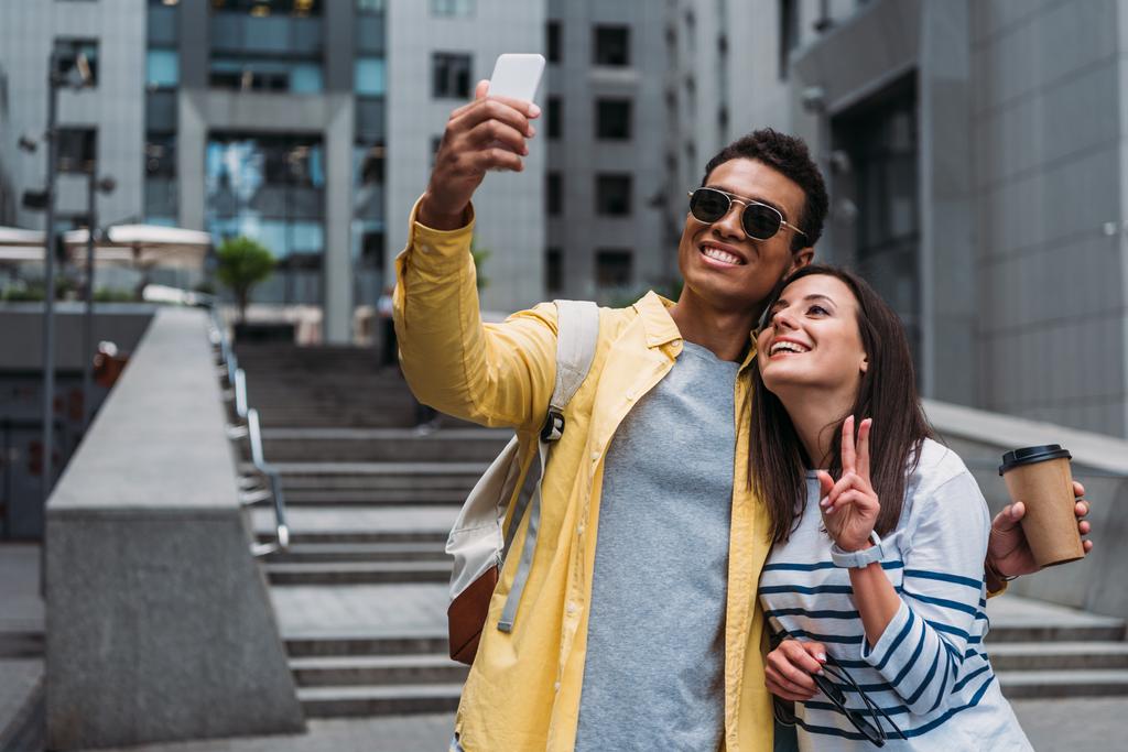 BI-rasowy mężczyzna w okularach z kobietą biorąca selfie na smartfonie - Zdjęcie, obraz