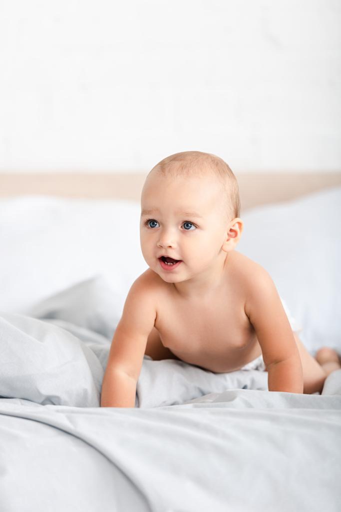 Criança pequena bonito rastejando em roupas de cama brancas e olhando para longe
 - Foto, Imagem